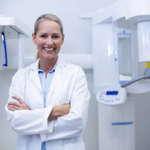 Smiling dentist with arms crossed, dental X-ray machine.