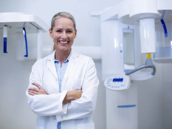 Smiling dentist with arms crossed, dental X-ray machine.