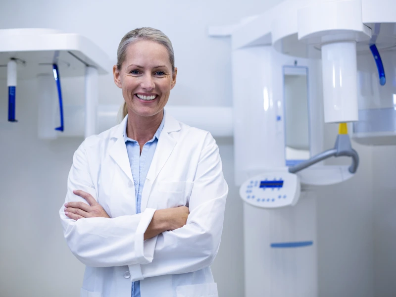 Smiling dentist with arms crossed, dental X-ray machine.