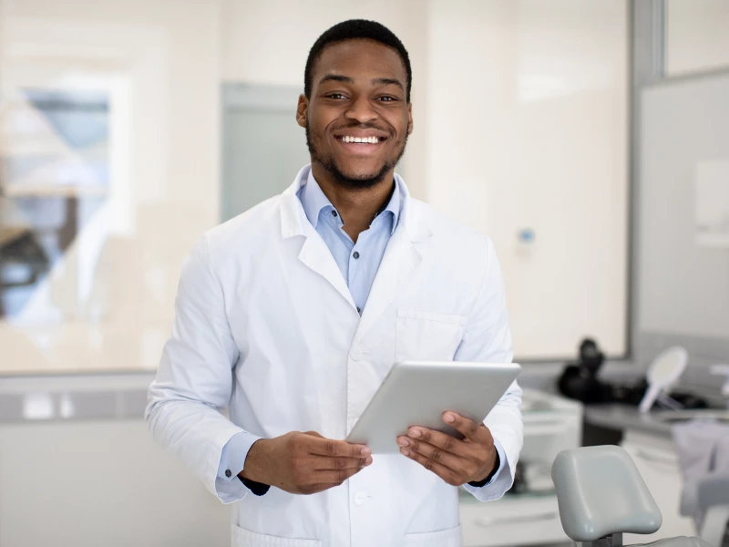 Smiling doctor holding tablet in clinic.