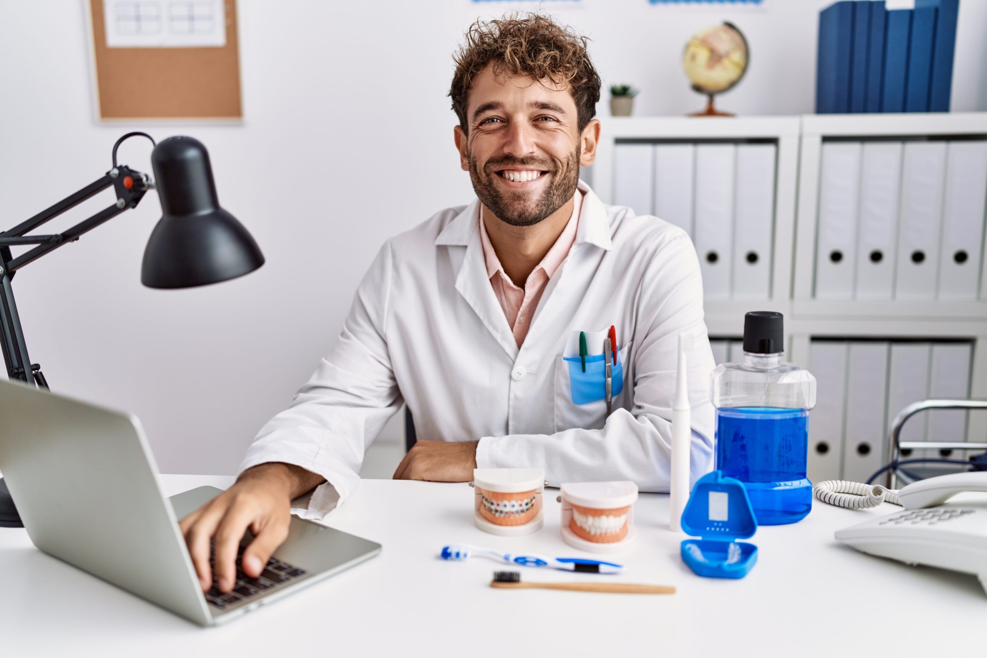 Young hispanic dentist man working at medical clinic with a happy and cool smile on face. lucky person. A man sitting at his desk with a laptop